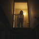 A woman stands at the top of a dark staircase with a light behind her.